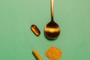 Golden spoon with three dietary supplement pills on a green background
