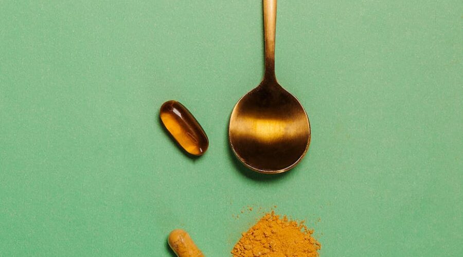 Golden spoon with three dietary supplement pills on a green background