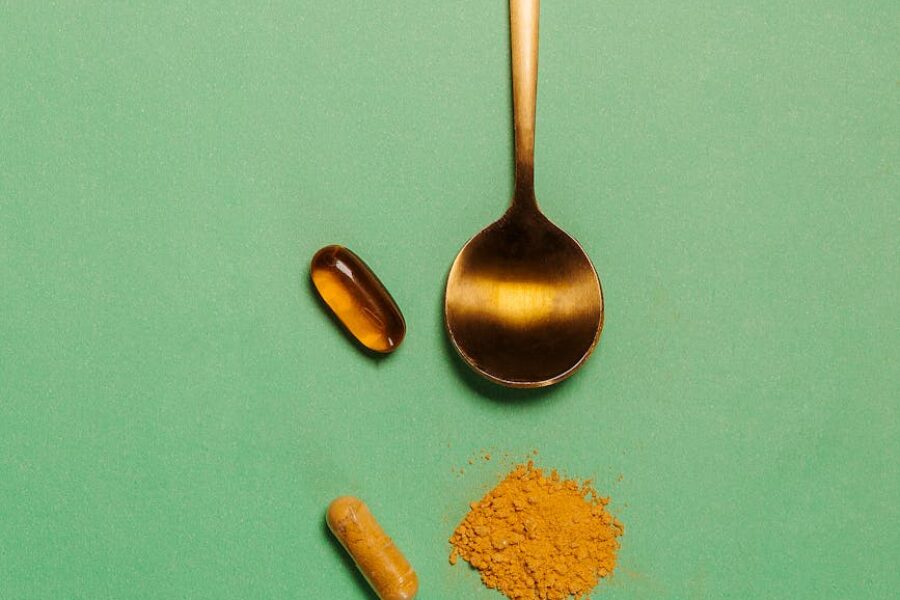 Golden spoon with three dietary supplement pills on a green background
